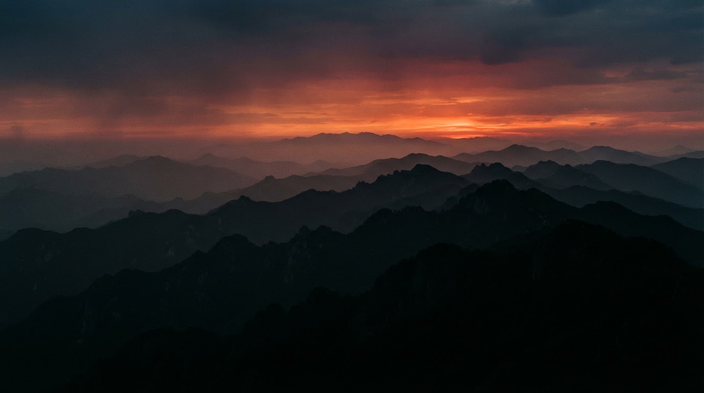 A sunset sky glowing red above the layered mountain ranges of Gangwon, only the ridgelines left in silhouette (AI-generated image)