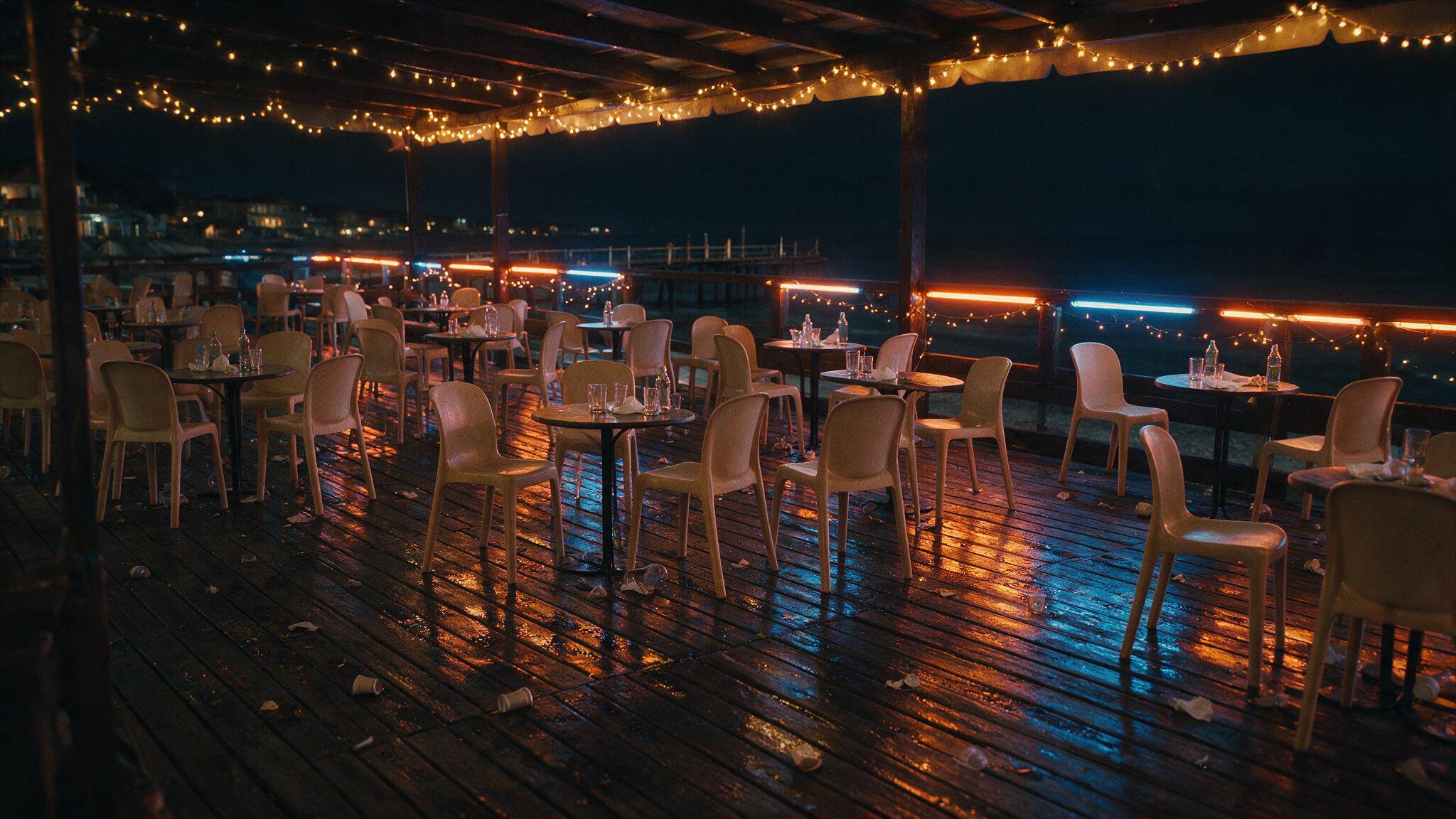 A dark seaside bar terrace at night on the Bulgarian coast, empty chairs, warm neon glow, no people, photorealistic (AI-generated image)