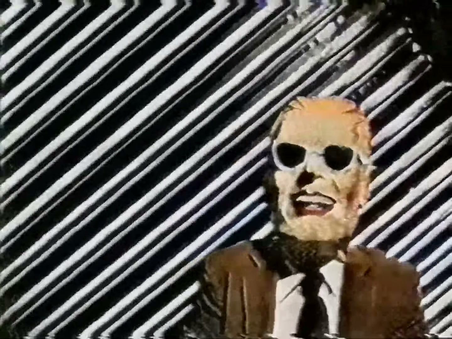 An actual capture of the intrusion that took over WTTW on the night of November 22, 1987 — the figure in the Max Headroom mask against a rotating striped backdrop