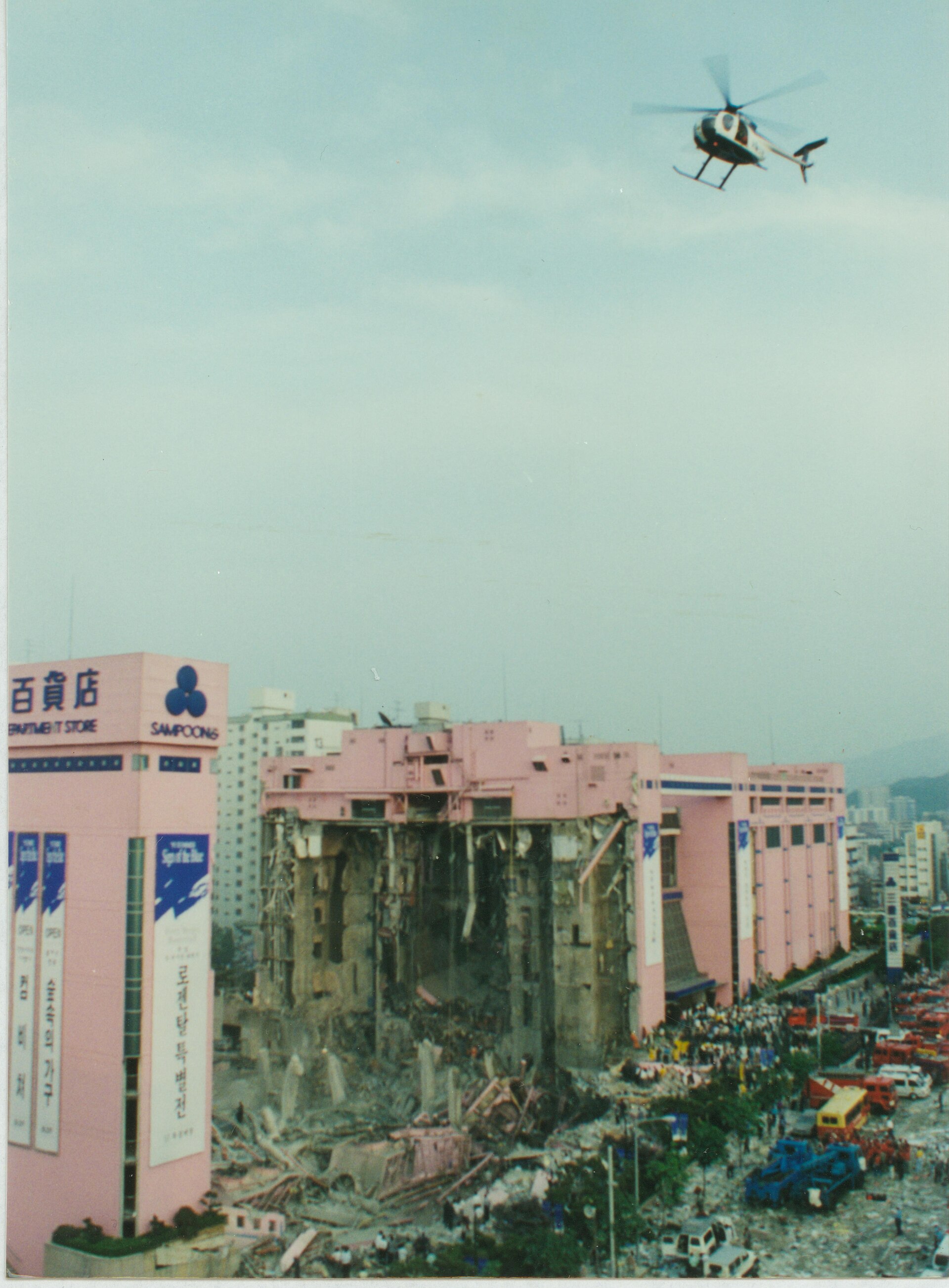 崩れ落ちた建物の側面と、その上空を旋回するヘリコプター（Wikimedia Commons）
