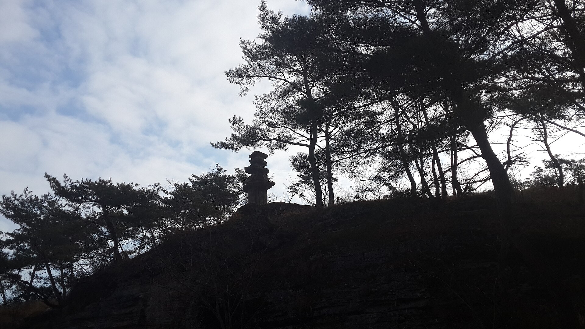 尾根の上にただ一基だけ立つ石塔のシルエット — 逆光の中に浮かぶ雲住寺の谷の実景