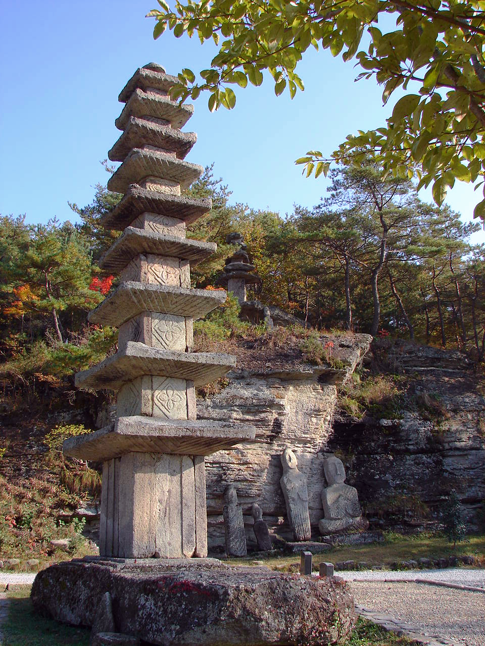 和順・雲住寺の九層石塔と、その背後の岩壁の下に並ぶ摩耗した石仏群 — 現場の実景